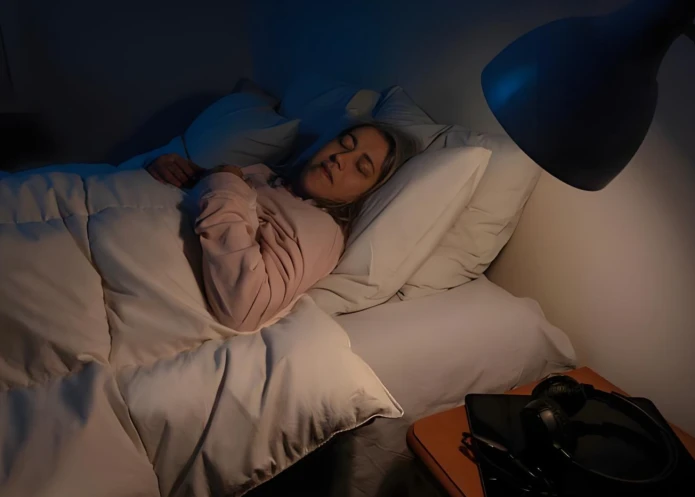 A young person lying on their side in bed with eyes closed, looking relaxed